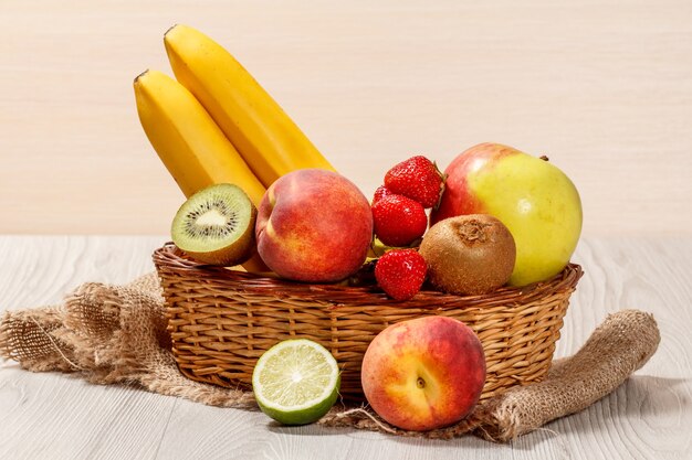 Frische Erdbeeren, Nektarine, Limette, Kiwi, Banane, Apfel in einem Weidenkorb auf einem Holztisch