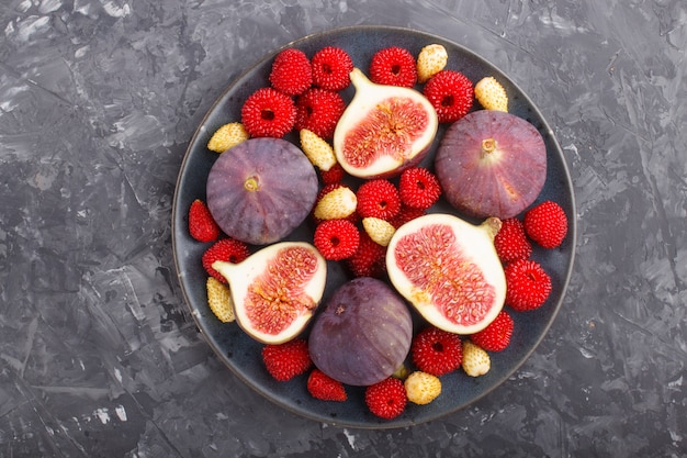 Frische Feigen, Erdbeeren und Himbeeren auf blauer Platte auf schwarzem konkretem Hintergrund