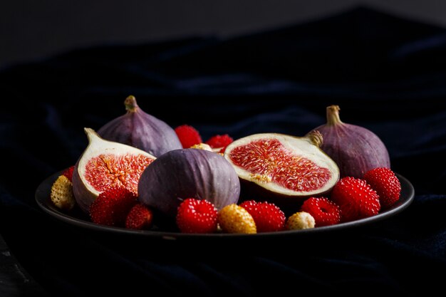 Frische Feigen, Erdbeeren und Himbeeren auf blauer Platte und blauem Samtgewebe