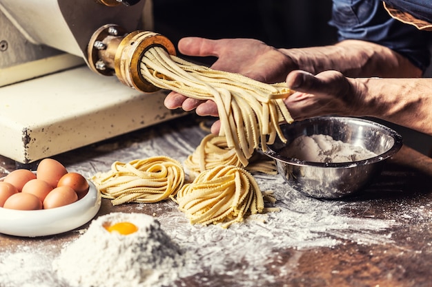 Frische Fettuccine-Eierteig-Nudelnester und die Hände des Küchenchefs halten eine weitere Dosis der italienischen Spezialität.