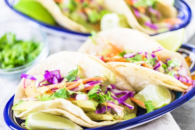 Frische Fisch-Tacos mit Gemüse und Guacamole-Salsa auf weißen Maistortillas.