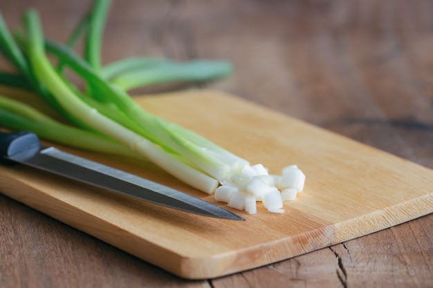 Frische Frühlingszwiebel und Küchenmesser setzten an Holzschneidebrett auf hölzerne Tabelle.