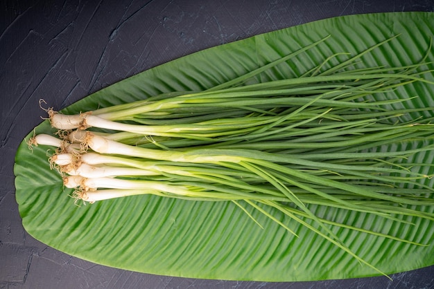 Frische frühlingszwiebeln im bananenblatt auf holzuntergrund