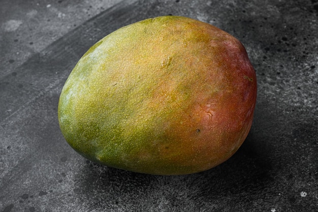 Frische ganze Mangofrüchte auf schwarzem, dunklem Steintischhintergrund