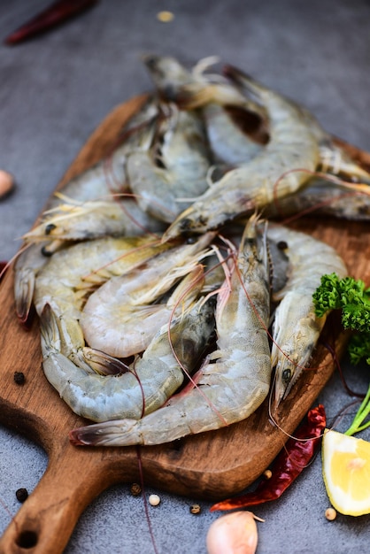 Frische Garnelen Garnelen zum Kochen mit Gewürzen Zitrone Knoblauch schwarzer Pfeffer Chili auf Holzschneidebrett im Fischrestaurant Rohe Garnelen auf dunklem Teller