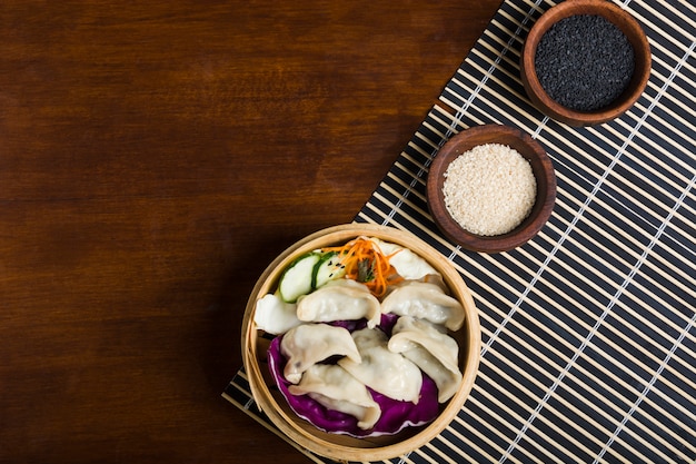 Frische gekochte Gyoza-Mehlklöße innerhalb der heißen Dampfer mit Schwarzweiss-Samen des indischen Sesams auf Holztisch