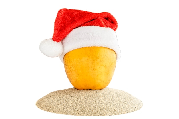 Frische gelbe Kokosnuss in einer roten Weihnachtsmannmütze auf Sand. Tropisches Sommerkonzept des Feiertags.