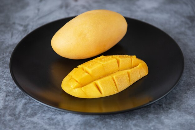 Frische gelbe Mangofrucht in einem schwarzen Teller