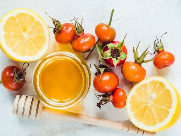 Frische gelbe Zitrone, Krug Honig und rote Beeren auf einem weißen Holztisch. Draufsicht, Nahaufnahme, isoliert. Konzept zur Vorbeugung von Erkältungen