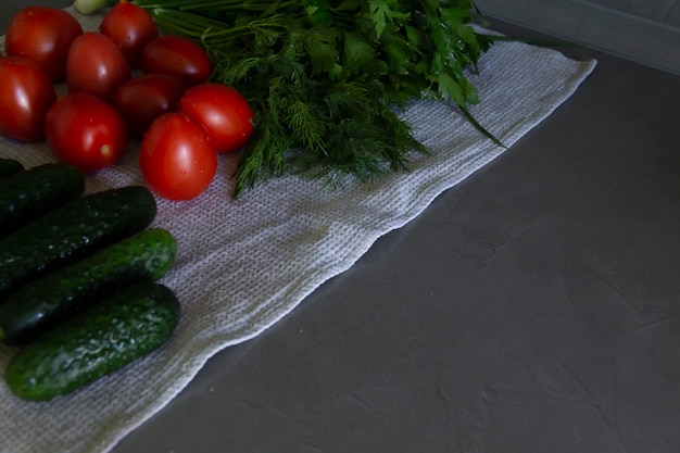 Frische Gemüsegurken, Tomaten und Gemüse mit Dill und Petersilie liegen auf der grauen Oberfläche der Küche auf einem Leinentuch