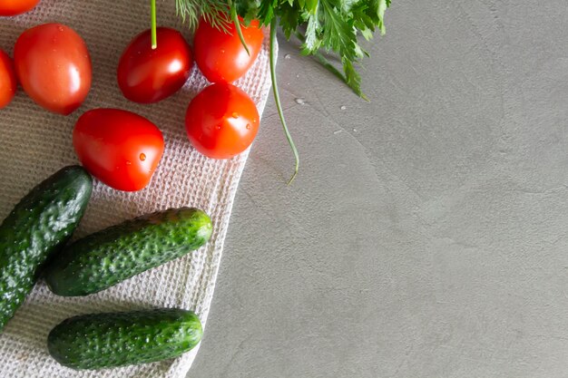 Frische Gemüsegurken, Tomaten und Gemüse mit Dill und Petersilie liegen auf der grauen Oberfläche der Küche auf einem Leinentuch