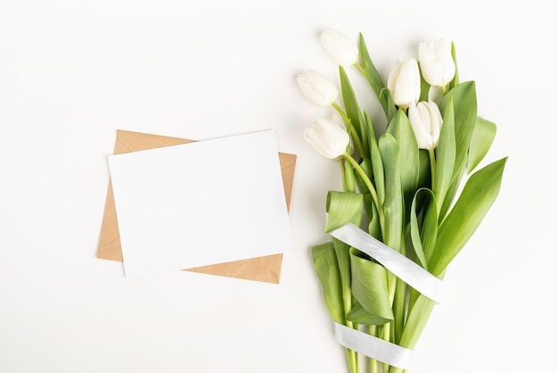 Frische geschnittene weiße Tulpenblumen und leere Karte mit Umschlag Draufsicht auf weißem Hintergrund