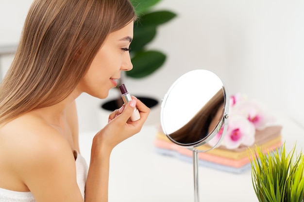 Frische gesunde Haut der schönen Frau, die auf Spiegel schaut, macht Make-up