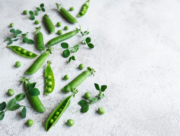 Frische grüne Erbsenschoten und grüne Erbsen mit Sprossen auf konkretem Hintergrund. Konzept der gesunden Ernährung, frisches Gemüse.