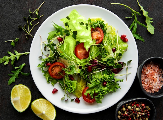 Frische grüne gemischte Salatschüssel mit Tomaten und Mikrogrün auf schwarzem Betontisch. Gesundes Essen, Draufsicht.