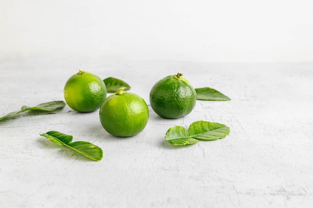 Frische grüne Limette und Limettenblätter auf weißem Holztisch