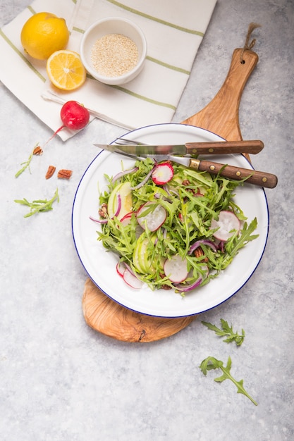 Frische grüne Rucola-Blätter auf weißer Schüssel, Rucola-Rucola-Salat mit Apfel, Radieschen, Pekannüssen, Zwiebel auf rustikalem Holzhintergrund mit Platz für Text. Draufsicht, gesundes Essen, Diät. Ernährungskonzept