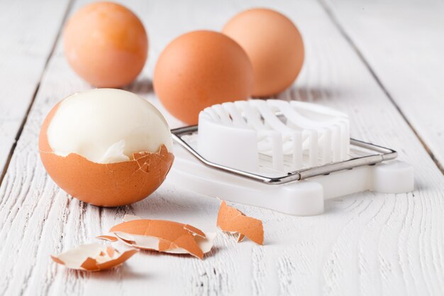 Frische hart gekochte Eier mit Schale daneben auf Holzbrett (Selektiver Fokus, Fokus auf der Vorderseite der Schale beim ersten Ei)