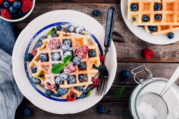 Frische hausgemachte belgische Waffeln mit Heidelbeeren und Himbeeren zum Frühstück auf Holzhintergrund