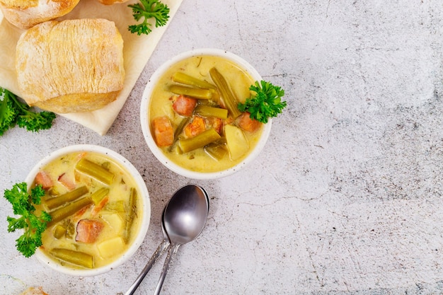 Frische hausgemachte cremige Gemüsesuppe auf weißer Schüssel mit Abendessenrolle und Löffel.