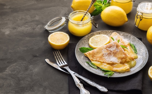 Frische hausgemachte Crepes mit Zitronenquark auf grauer Betonoberfläche. Selektiver Fokus.