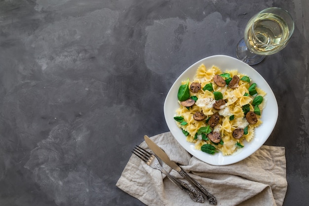 Frische hausgemachte Farfalle-Nudeln mit Pilzen und Spinat auf Betonuntergrund