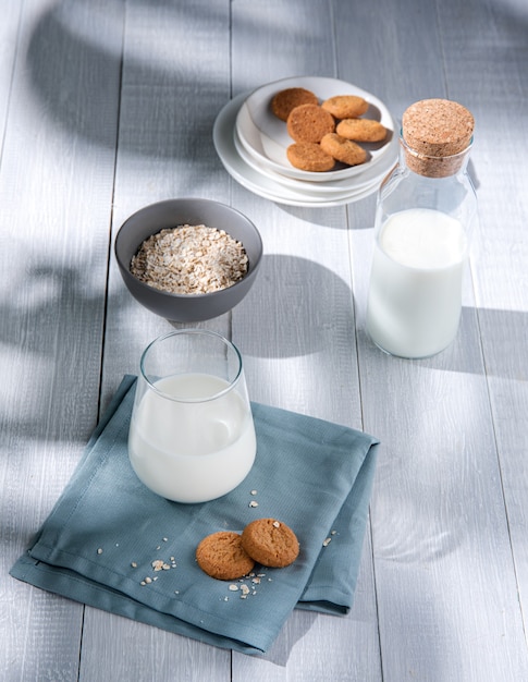 Frische hausgemachte Haferkekse mit einem Glas veganer Milch auf einem weißen Holztisch. Morgenlicht