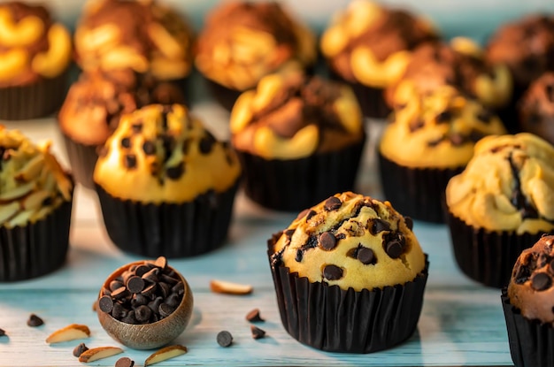 Frische hausgemachte köstliche Vanille- und Schokoladenmuffins in Cupcake-Halter aus Papier mit Plätzchen und Sahne isoliert auf Serviettentischdecke im Hintergrund