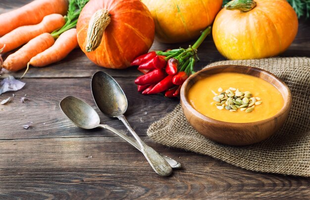 Frische hausgemachte Kürbissuppe mit Zutaten auf rustikalem Holztisch.