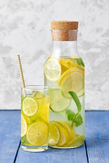 Frische hausgemachte Limonade mit Limette und Minze im Glas mit Papierstroh und Flasche auf hellblauem Hintergrund
