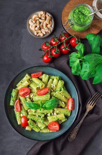 Frische hausgemachte Tortiglioni-Nudeln mit veganer Pesto-Sauce, Cashewnüssen und Kirschtomaten auf grauem Betonhintergrund. Draufsicht.