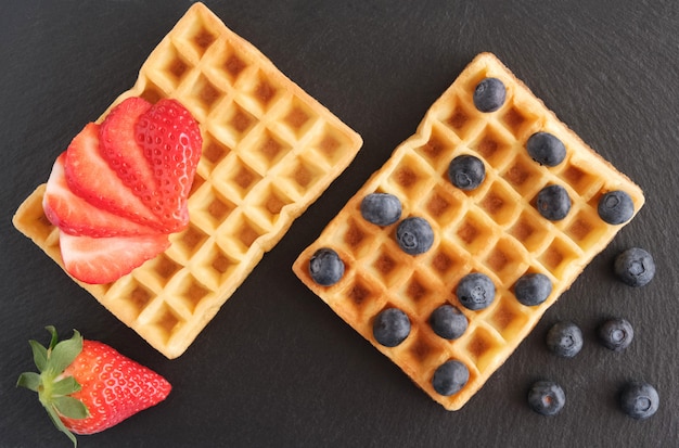 Frische hausgemachte Wiener oder belgische Waffeln mit frischen Erdbeeren und Blaubeeren auf Schwarz