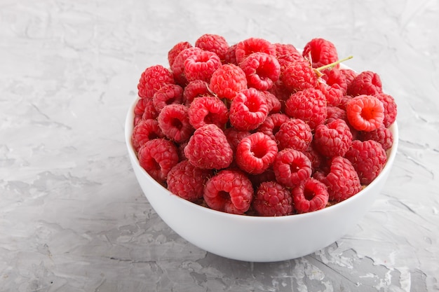 Frische Himbeere in der weißen Schüssel auf grauem konkretem Hintergrund. Seitenansicht.