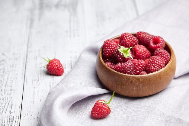 Frische Himbeeren in der Holzschale auf grauem Tisch mit Leinenserviette