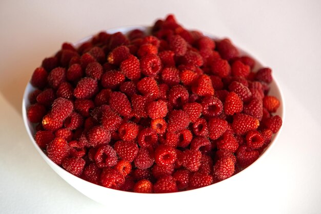 Frische Himbeeren in einer weißen Schüssel lokalisiert auf weißem Tabellenhintergrund Beschneidungspfad eingeschlossen