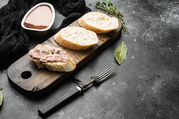 Frische Hühnerleberpastete aus der Dose auf Brot auf schwarzem, dunklem Steintischhintergrund mit Kopierraum für Text