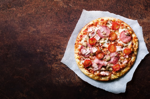 Frische italienische Pizza mit Champignons, Schinken, Tomaten, Käse auf Trägerpapier,