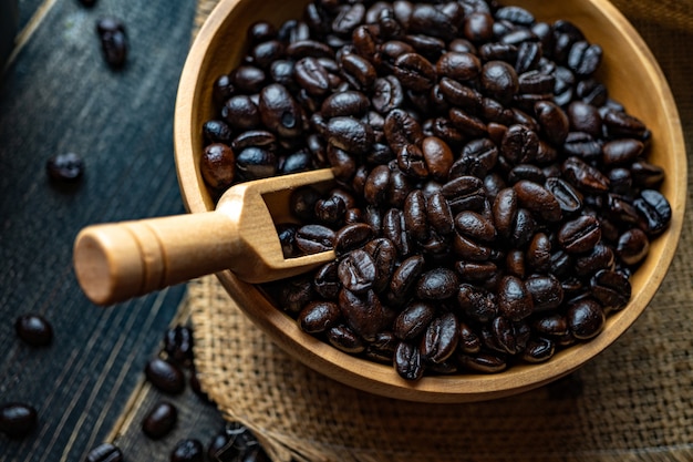 Frische Kaffeebohnen in der Holzschale auf einem Beutel aus Sackleinen auf einer Holzoberfläche.