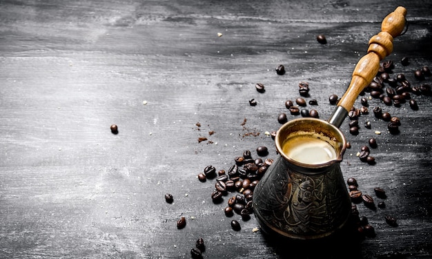 Frische Kaffeekanne mit Körnern herum auf schwarzer Tafel.