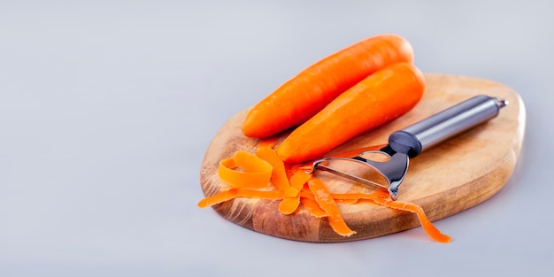 Frische Karotte mit Schäler am Holzbrett auf grauem Hintergrund, Fahnenentwurf. Gemüse für eine gesunde Ernährung.