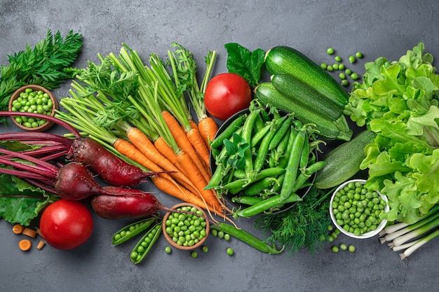 Frische Karotten, Rüben, Zucchini. Erbsen, Tomaten und Grün auf blauem Grund. Kulinarisches Gemüse Hintergrund. Ansicht von oben.