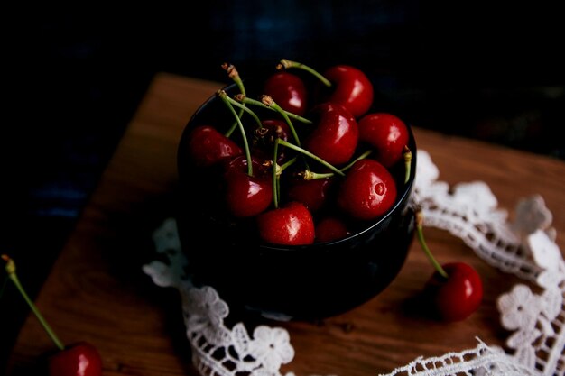 Frische Kirsche in Glasschale auf dem Sackleinen auf schwarzem Hintergrund in einem Low-Key mit Spitzendekoration Rustikale Bio-Beeren aus eigenem Anbau Gemütliches Abendessen auf dem Land