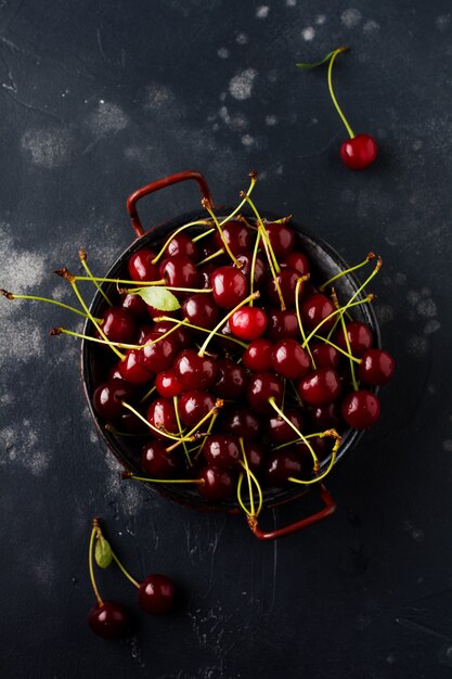 Frische Kirschenbeeren in der schwarzen Keramikplatte auf der alten Oberfläche des dunklen Betons. Draufsicht.