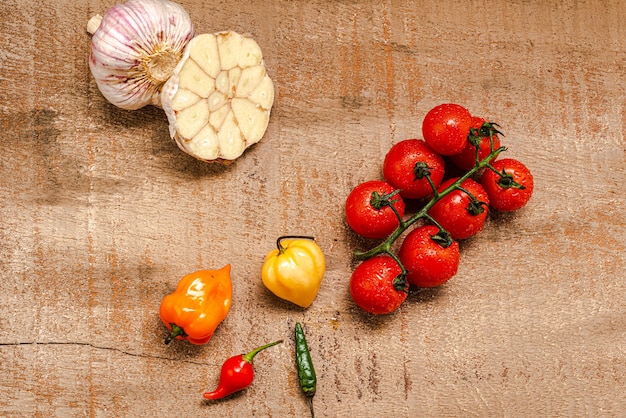 Frische Kirschtomaten auf rustikalem braunem Holzhintergrund mit mehreren Paprikaschoten und in Scheiben geschnittenem Knoblauch...