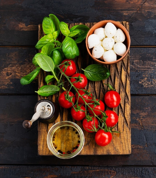 Frische Kirschtomaten, Basilikumblätter, Mozzarella und Olivenöl auf altem Holzhintergrund. Zutaten für den Caprese-Salat. Selektiver Fokus.