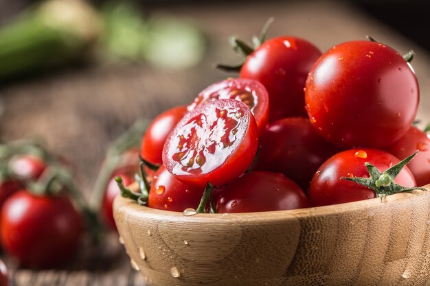 Frische Kirschtomaten in Holzschale auf altem Eichentisch.