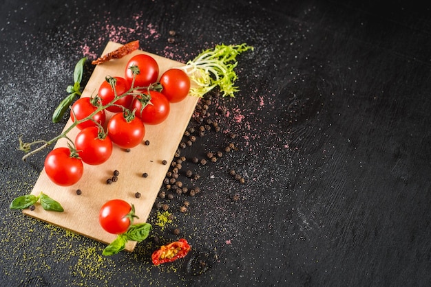 Frische Kirschtomaten mit Gewürzen auf schwarzem Hintergrund