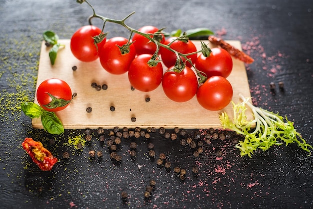 Frische Kirschtomaten mit Gewürzen auf schwarzem Hintergrund