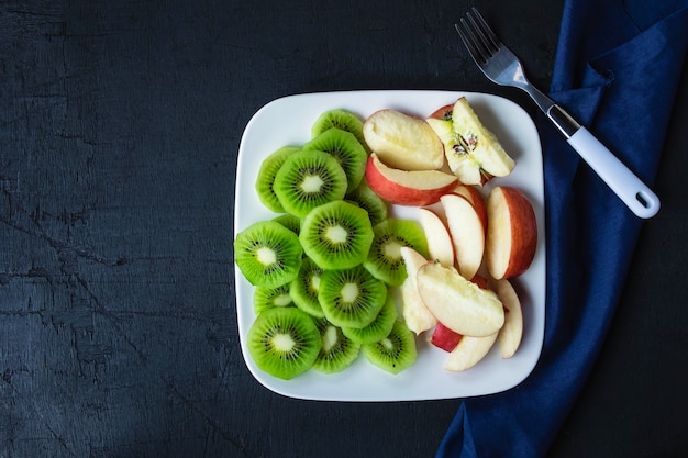 Frische Kiwi und Äpfel der Mischfrucht mit Trauben in einer Platte auf einem Holztisch.