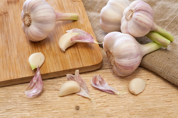 Frische Köpfe und Knoblauchzehen auf Schneidebrett und Holztisch